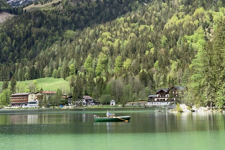 Ruhiger See, Hintersee, mit einem kleinen Boot und grünen, bewaldeten Hügeln im Hintergrund.