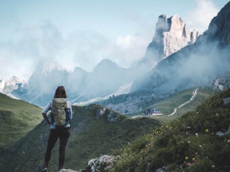 Frau mit Rucksack blickt auf eine bergige Landschaft mit Wolken.