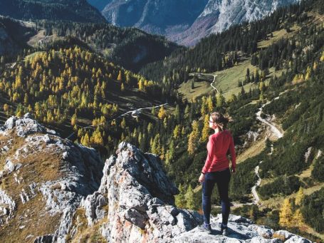Natalia Herzinger beim Wandern im Nationalpark Berchtesgaden Frau steht auf einem Felsen und blickt auf eine herbstliche Landschaft mit Bergen.