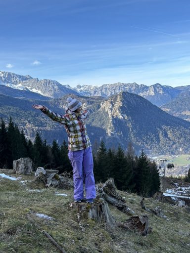 Natalia Herzinger steht auf einem Felsen in den Bergen und breitet die Arme aus bei einer Winterwanderung am Jenner.