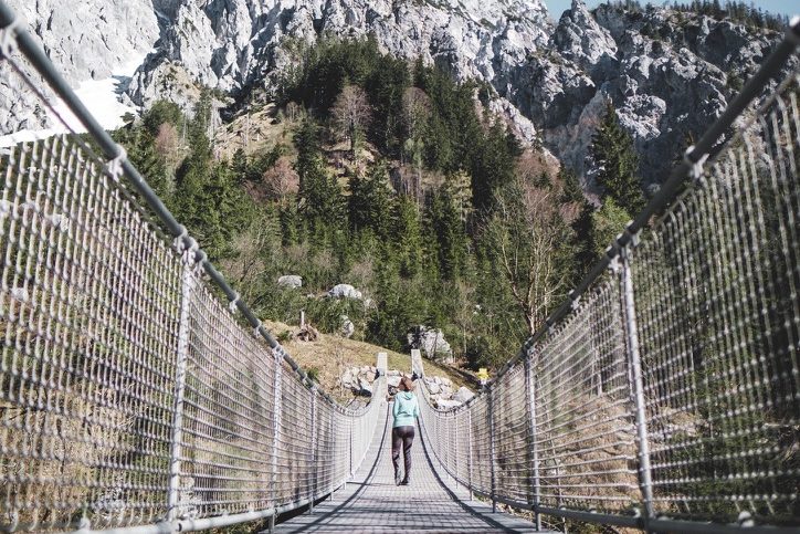 Frau auf einer Hängebrücke mit Bergen und Bäumen im Hintergrund im Nationalpark Berchtesgaden.