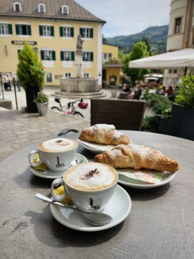 Zwei Cappuccinos und zwei Croissants auf einem Tisch in einem Café im Freien.