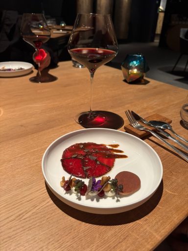 Ein kunstvoll angerichteter Teller mit Garnelen, Gemüse und einer Sauce auf einem Holztisch.