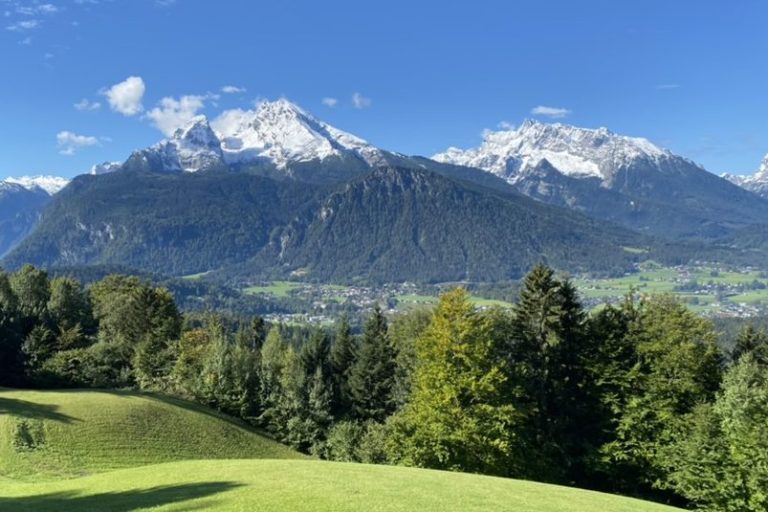 Schneebedeckte Berge Watzmann und Hochkalter mit grünem Tal und strahlend blauem Himmel.